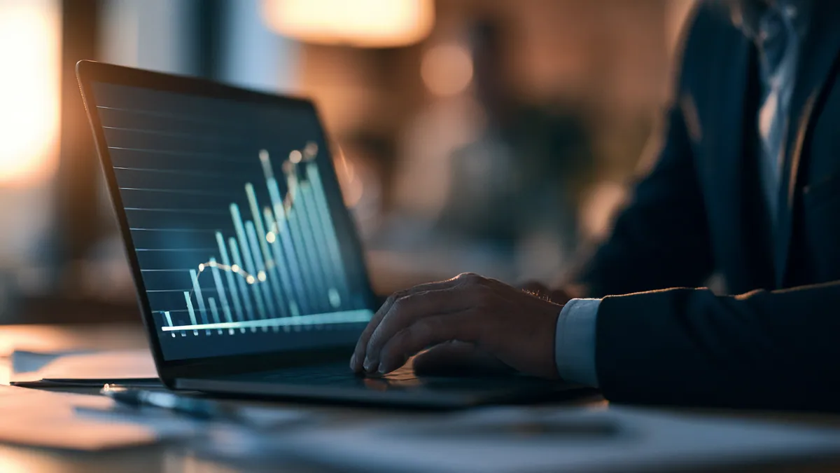 A person working on a laptop that shows a rising data chart