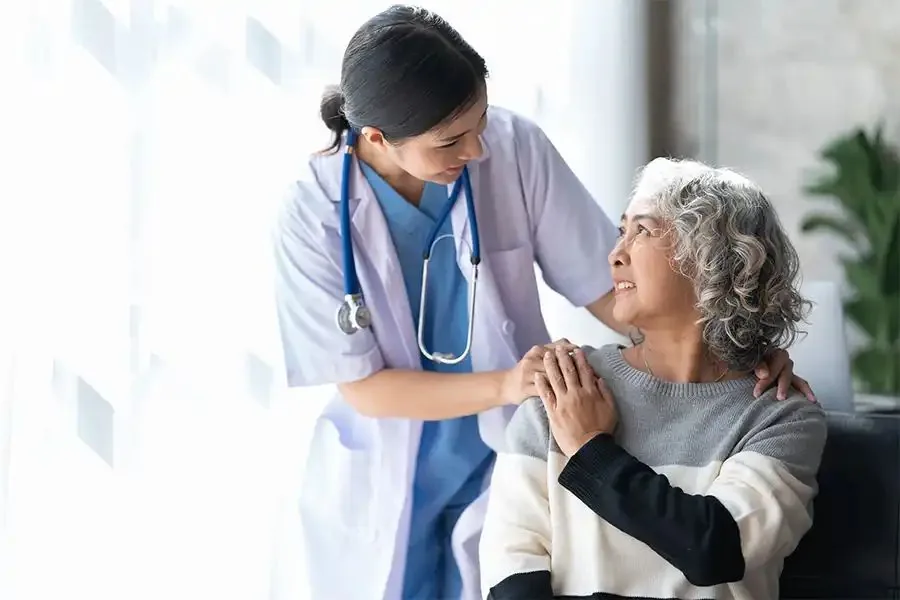 Caregivers helping an older man stand up from his bed at home